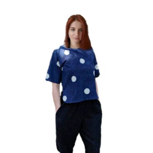 May include: A navy blue top with large white polka dots. The top has short sleeves and a wide neckline. The model is also wearing black pants. The outfit is casual and stylish.