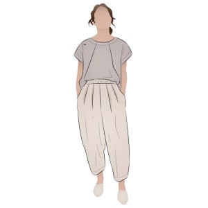 May include: A woman wearing a light purple short-sleeved shirt and beige pants with pleats. She is standing with her hands in her pockets.
