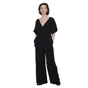 May include: A black jumpsuit with a V-neckline and a tie belt. The jumpsuit has short sleeves and wide legs.