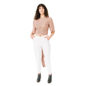 May include: A woman wearing a pink and black polka dot top with a white pair of pants and black ankle boots.