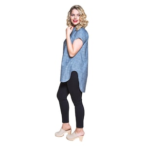 May include: A woman wearing a light blue collared shirt with short sleeves and black leggings. She is wearing beige clogs with a wooden heel.