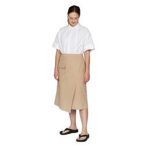 May include: A beige wrap skirt with a large pocket on the front. The skirt is knee-length and has a relaxed fit.