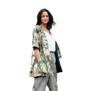 May include: A woman wearing a green and white floral print kimono-style jacket with a white top and gray pants.