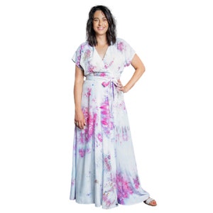 May include: A woman wearing a long, white wrap dress with a pink and purple tie-dye pattern. The dress has a V-neckline and short sleeves.