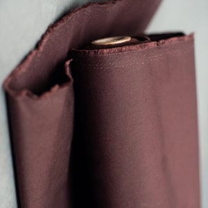 May include: A roll of dark brown fabric with a slightly textured surface. The fabric is rolled up and the end is folded over.