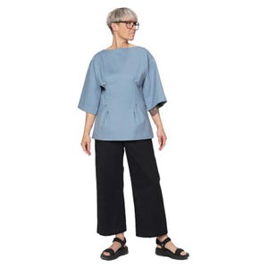 May include: A light blue top with a boat neck and three-quarter sleeves, paired with black wide-leg pants and black sandals. The top has a fitted waist and pleats. The outfit is simple and modern.