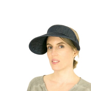 May include: A dark blue denim visor with a wide brim. The visor is angled to the side and is worn by a person with light brown hair.