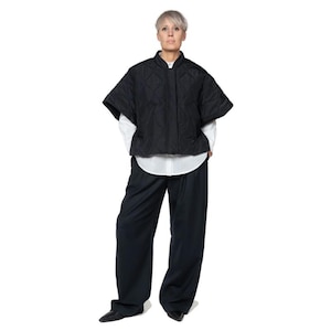 May include: A black quilted short-sleeved jacket with a stand-up collar and a zipper closure. The jacket is worn over a white button-down shirt and dark blue pants.