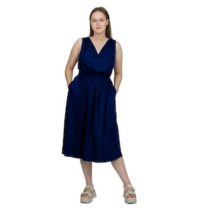 May include: A sleeveless, navy blue dress with a V-neckline and a gathered waist. The dress has a knee-length skirt and pockets. The person is wearing white platform sandals.