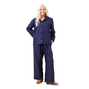 May include: Navy blue pajama set with vertical white pinstripes. The long-sleeved button-down shirt has a chest pocket. The matching wide-leg pants complete the set. The person is wearing patterned shoes.