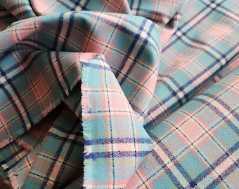 May include: A close-up of a fabric with a plaid pattern. The fabric features a combination of light blue, pink, and gray colors, with dark blue lines creating the plaid design. The fabric is folded and draped, showing the texture and pattern.