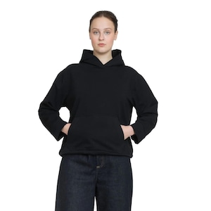 May include: A black hoodie with a kangaroo pocket and a hood. The long-sleeved sweatshirt is worn with dark blue denim pants. The model is standing in front of a white background.