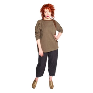 May include: A woman wearing a brown, long-sleeved sweater with a brown patch on the right shoulder. She is wearing black pants with a white polka dot pattern and gold shoes.