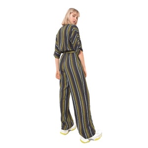 May include: A woman wearing a black and green striped jumpsuit with a wide leg. The jumpsuit has a belt and short sleeves.