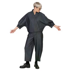 May include: A dark charcoal denim two-piece set consisting of a wrap-style top with wide, three-quarter length sleeves and matching cropped, wide-leg trousers. The outfit is paired with black lace-up shoes and clear-framed glasses.