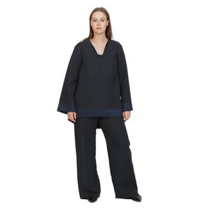 May include: A navy blue two-piece outfit. The top is a long-sleeved tunic with a V-neck and dark blue trim at the cuffs and hem. The matching pants are wide-legged. The outfit is made of a soft, flowing fabric.
