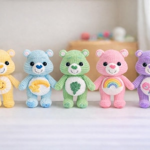 May include: Five colorful crochet teddy bears in yellow, blue, green, pink, and purple. Each bear has a unique belly design, including a smiling sun, a shooting star, a four-leaf clover, a rainbow, and a pair of lollipops. The bears are standing upright.