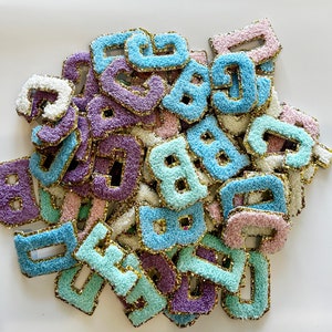 May include: A pile of colorful felt letters with gold glitter trim. The letters are in various shades of blue, purple, pink, and green.
