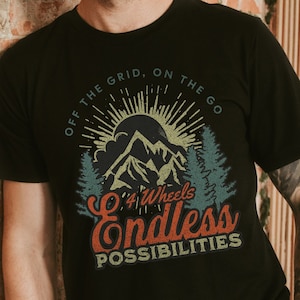 May include: Black t-shirt with a vintage-style graphic of a mountain range with a sun and trees. The text reads "Off the grid, on the go 4 Wheels Endless Possibilities".