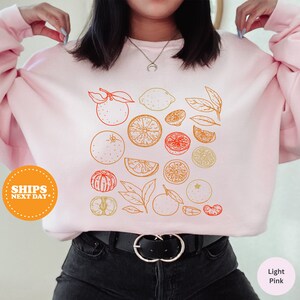 a woman wearing a pink sweatshirt with oranges on it