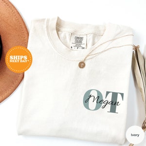 May include: Ivory t-shirt with the text "OT Megan" in a light green color. The shirt is folded and has a tag that says "Comfort Colors".