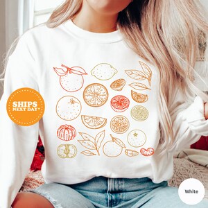 a woman wearing a white shirt with oranges and lemons on it