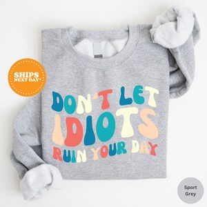 a gray shirt with the words don't let idiots run your day on it