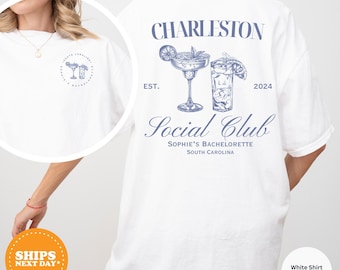 May include: White t-shirt with blue text that reads "Charleston Est. 2024 Social Club Sophie's Bachelorette South Carolina". The shirt also features a graphic of two cocktail glasses.