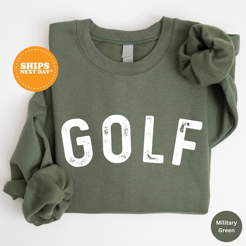 Puede incluir: Una sudadera verde con la palabra "GOLF" impresa en blanco en la parte delantera. La sudadera tiene un aspecto desgastado y vintage.