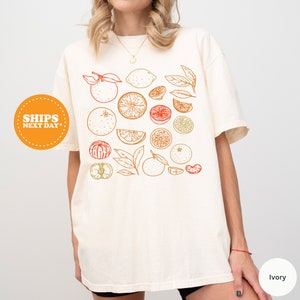 a woman wearing a white t - shirt with fruit on it