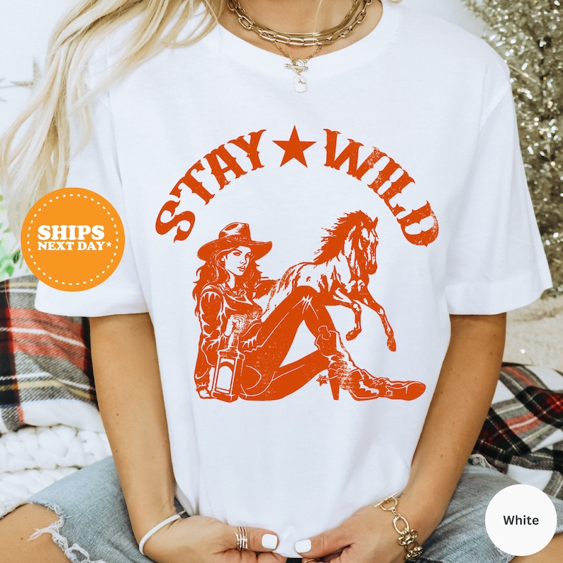 a woman wearing a white shirt with an orange graphic of a cowboy riding a horse