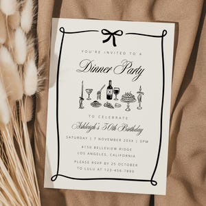 Könnte beinhalten: Eine cremefarbene Einladung mit schwarzem Text und Illustrationen für ein Abendessen. Die Einladung enthält den Text "Sie sind zu einem Abendessen eingeladen" und Details für Ashleighs 30. Geburtstag. Die Einladung befindet sich auf einem braunen Stoffhintergrund.