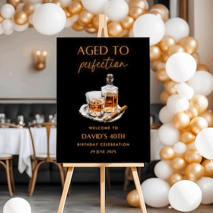 May include: A black sign on a wooden easel with the text "AGED TO perfection" in gold script. Below is an illustration of a whiskey bottle, a glass of whiskey, and a cigar. The sign reads "WELCOME TO DAVID'S 40TH BIRTHDAY CELEBRATION 29 JUNE 202X".