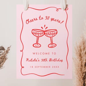 May include: A pink birthday sign with red text and a decorative border. The sign reads "Cheers to 30 years!" and "Welcome to Natalie's 30th Birthday, 18 September 20XX." Two champagne glasses are illustrated above the text.