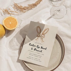 May include: A beige invitation card with a watercolor illustration of a bunny's ears and a bow. The text on the card reads "Join us for a Easter Egg Hunt & Brunch" with the date, time, address, and RSVP information.