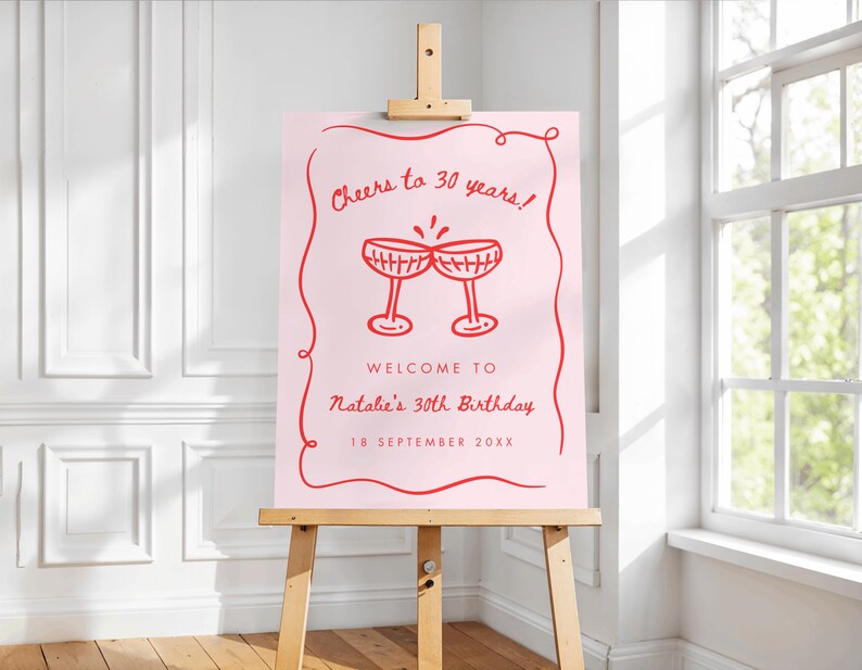 May include: A pink sign on a wooden easel with red text and illustrations. The sign reads "Cheers to 30 years!" and "Welcome to Natalie's 30th Birthday, 18 September 20XX." Two champagne glasses are illustrated in the center.