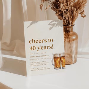 May include: A birthday invitation with the text "cheers to 40 years!" in a stylish font. The invitation includes details for John's 40th birthday celebration, featuring a beer mug illustration. A vase with dried flowers is in the background.