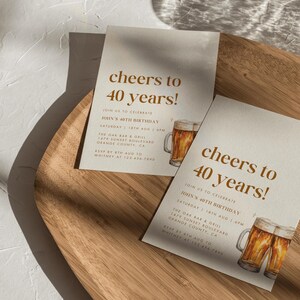 May include: Two invitation cards with the text "cheers to 40 years!" in brown. The cards include details for John's 40th birthday, a watercolor illustration of beer mugs, and event information.