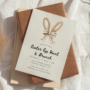 May include: A white invitation card with a watercolor illustration of bunny ears and a bow. The text on the card reads "Join us for a Easter Egg Hunt & Brunch, Saturday 17 April 2PM, 1425 Camden Avenue, Orange County, CA, RSVP by 5 April to Amanda at 123-456-7890".