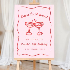 May include: A pink sign on an easel with red text that reads "Cheers to 30 years!" and "Welcome to Natalie's 30th Birthday, 18 September 20XX." Two red champagne glasses are drawn above the text.