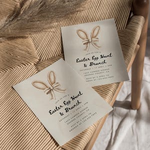 May include: Two light brown invitation cards with a watercolor illustration of bunny ears and a bow. The text on the cards reads "Join us for a Easter Egg Hunt & Brunch" with the date, time, and location details.