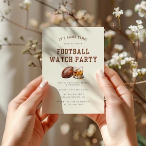 May include: A beige invitation card with brown text that reads "It's Game Time! Join us for a Football Watch Party". The card also includes a drawing of a football and a glass of whiskey.