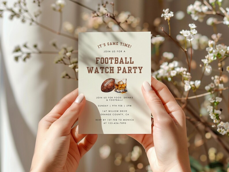 May include: A beige invitation card with brown text that reads "It's Game Time! Join us for a Football Watch Party". The card also includes a drawing of a football and a glass of whiskey.