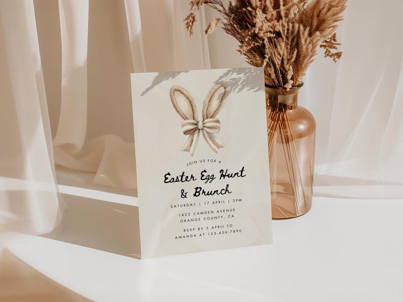May include: A light brown invitation card with a watercolor illustration of bunny ears with a bow. The text on the card reads "Join us for a Easter Egg Hunt & Brunch" with the date, time, and location details below.