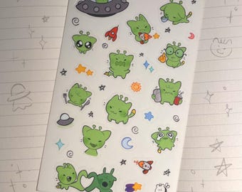 Puede incluir: Una hoja de pegatinas con ilustraciones de extraterrestres verdes en varias poses. Las pegatinas incluyen extraterrestres en una nave espacial, sosteniendo comida y con accesorios. El fondo es una página de cuaderno con garabatos. El nombre del artista es visible.