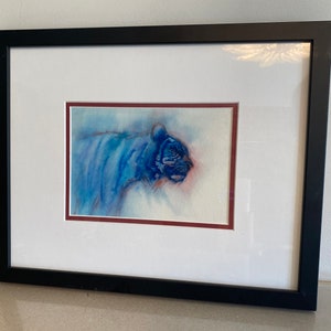 May include: A framed watercolor painting of a blue tiger. The tiger is facing to the right and is painted in a soft, abstract style. The background is a light blue and white.