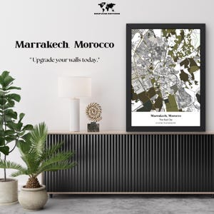 May include: A framed map print of Marrakech, Morocco, in black and white with olive green accents. The text "Marrakech, Morocco" and "Upgrade your walls today" are displayed. The print is displayed above a black cabinet with a white lamp and decorative items.
