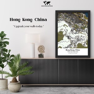 May include: A framed vertical map print of Hong Kong, China, featuring a stylized topographic and urban layout in shades of olive green, black, and white. The print includes the text Hong Kong, China, Where East Meets West, and coordinates.