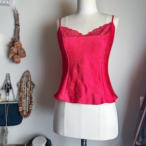 May include: A red satin top with a lace trim neckline. The top has thin straps and a fitted bodice.