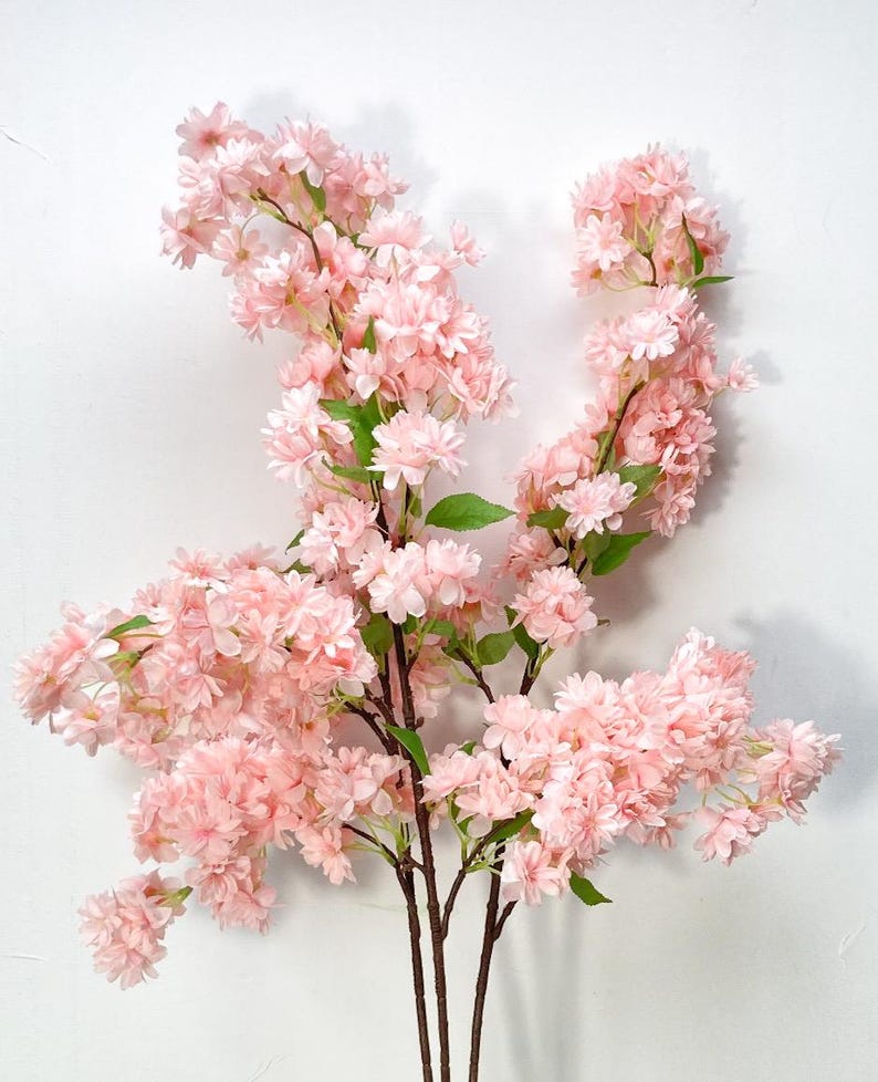 May include: A bouquet of artificial pink cherry blossom branches with multiple stems. The flowers are clustered together in a delicate, fluffy arrangement.